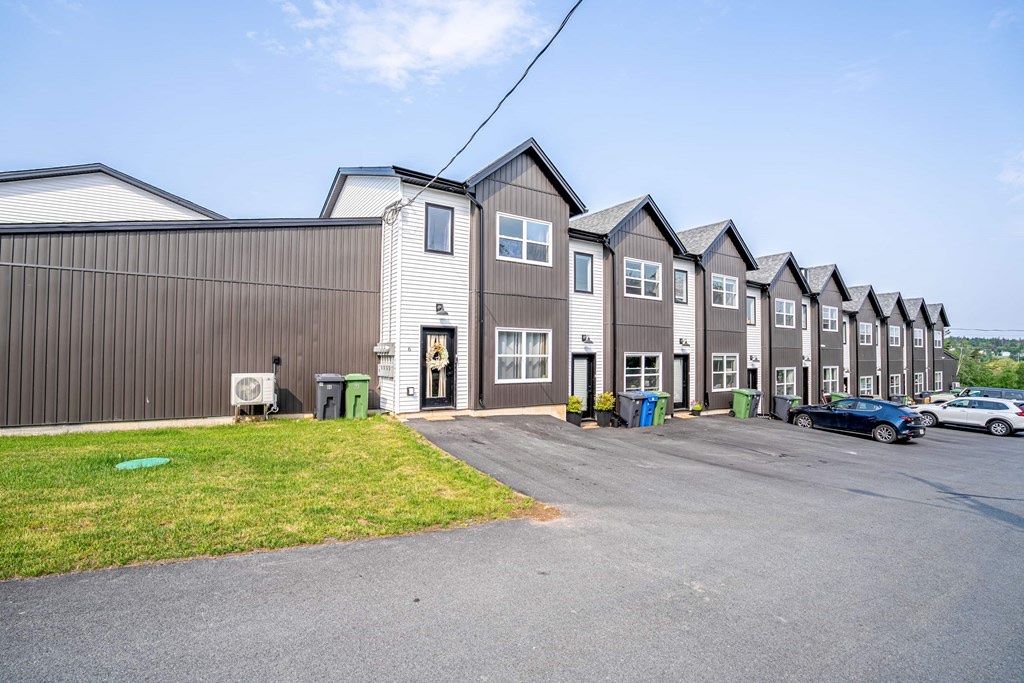 A row of two-storey townhomes with dark and white siding and gabled roofs, beside a paved parking area.